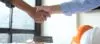 Two people shaking hands after applying for hard money loan. Hands are over a miniature home, documents, and a builders hat.