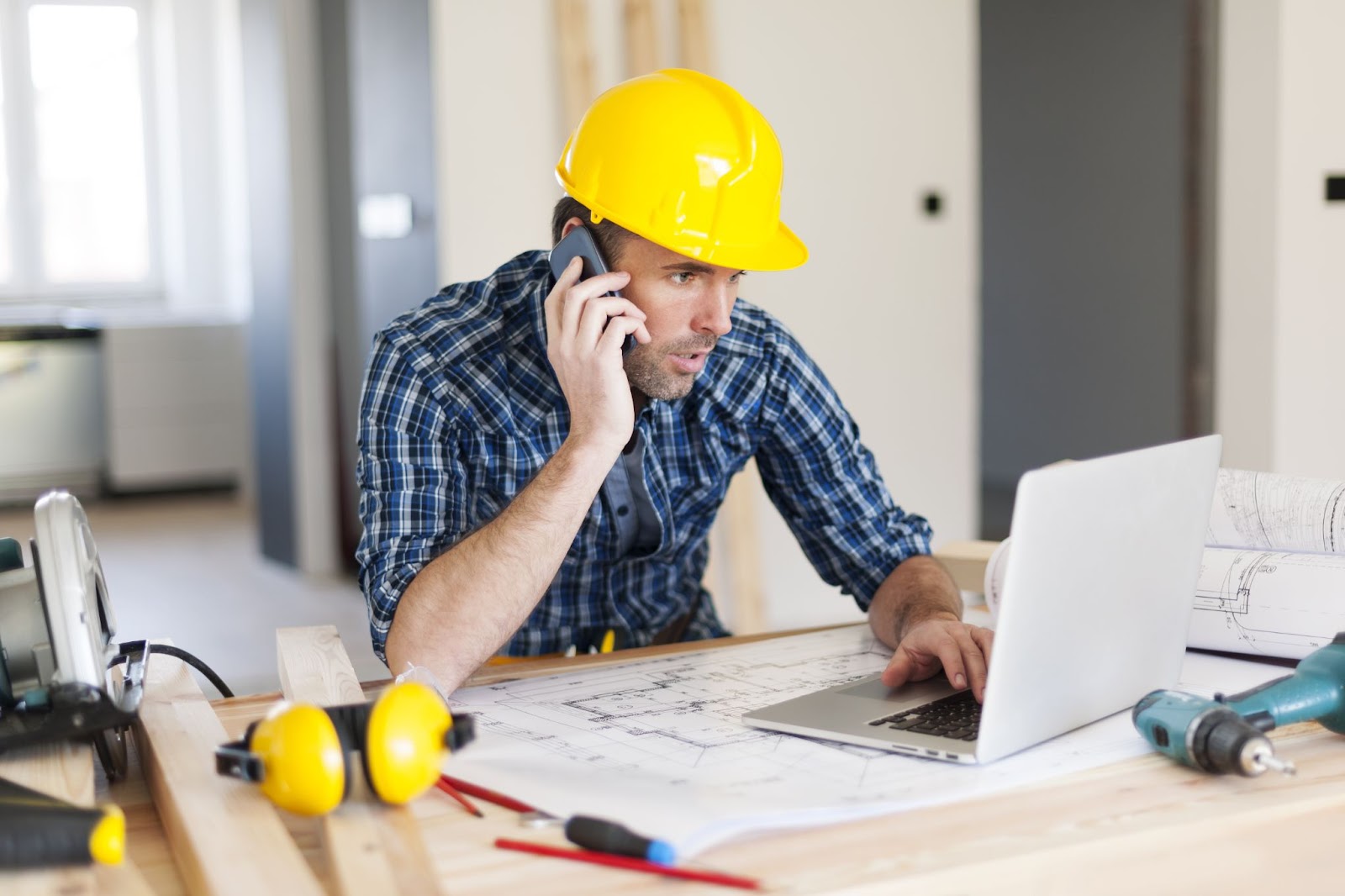 Man in hard hat reviews his finances as he talks to his lender about submitting a draw on his fix and flip project.